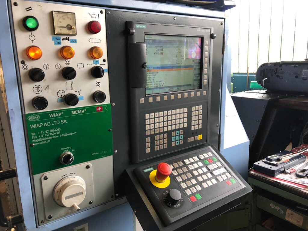 Bedienfeld einer CNC-Maschine mit Tasten, Schaltern und einem Monitor zur Anzeige von Betriebsdaten, mit Werkzeugen an der Seite.