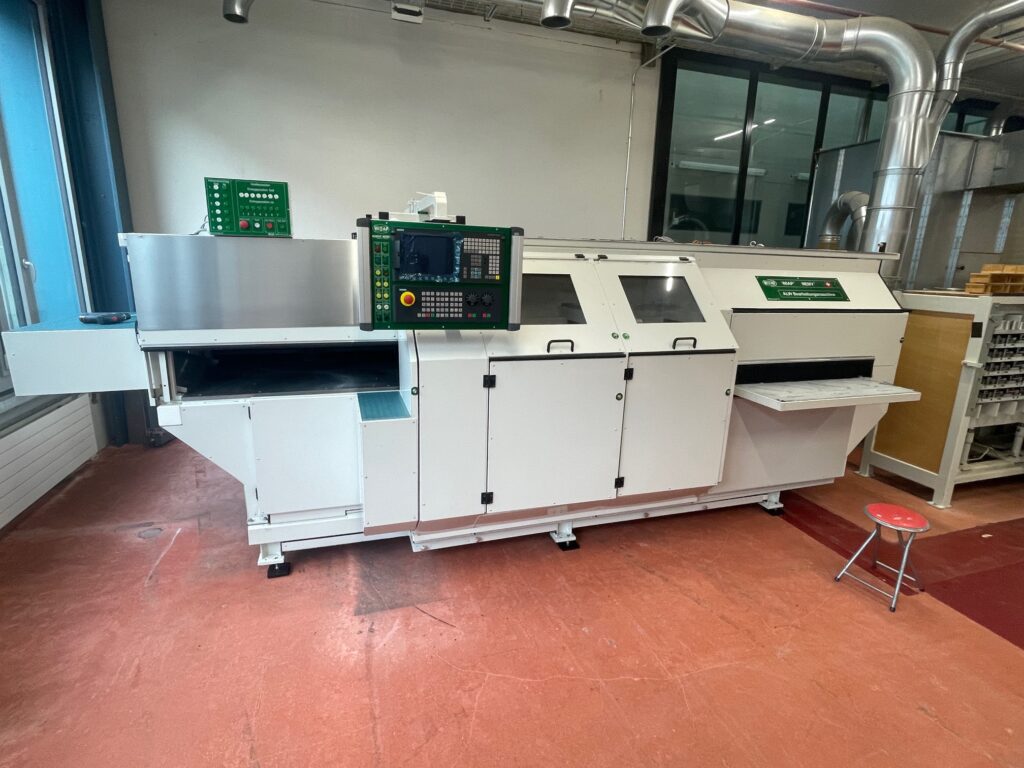Eine große, moderne Industriemaschine mit Bedienfeldern und Ladebereich, aufgestellt in einer gut beleuchteten Werkstatt mit rotem Bodenbelag.