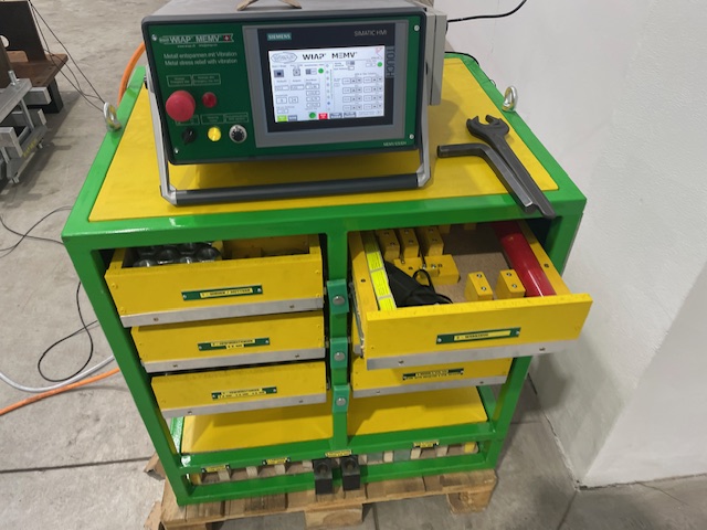 Ein grün-gelber Lagerwagen mit einem digitalen Monitor und mehreren Schubladen zur Aufbewahrung von Werkzeugen und Geräten in einer Werkstattumgebung.