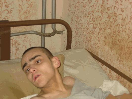 Photo: Ein liegender Patient in dem schmutzigen Zimmer, wo man dringend mal die Wände renovieren müsste.